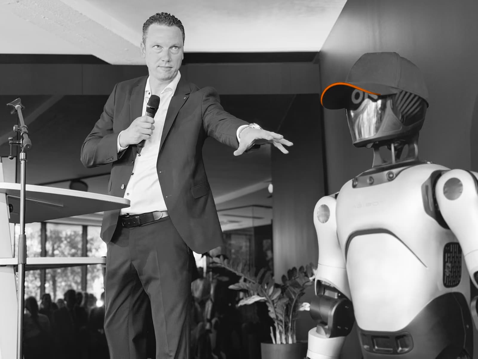 Mathias Dögel spricht bei einer Veranstaltung in ein Mikrofon, neben ihm ein humanoider Roboter.